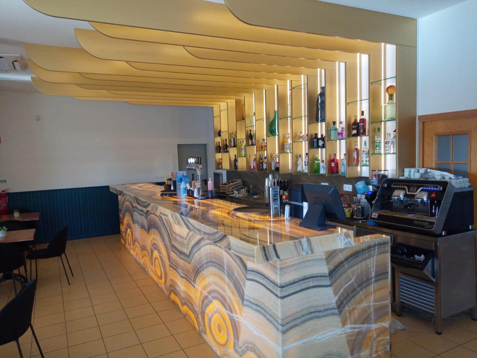 Bar de restaurante com balcão em pedra e estantes em madeira iluminadas
